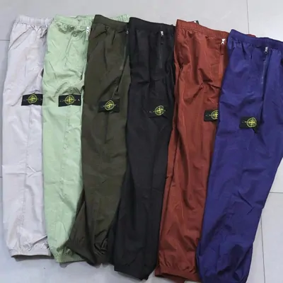 six nylon track pants in white, green, black, red and purple fanned on a floor
